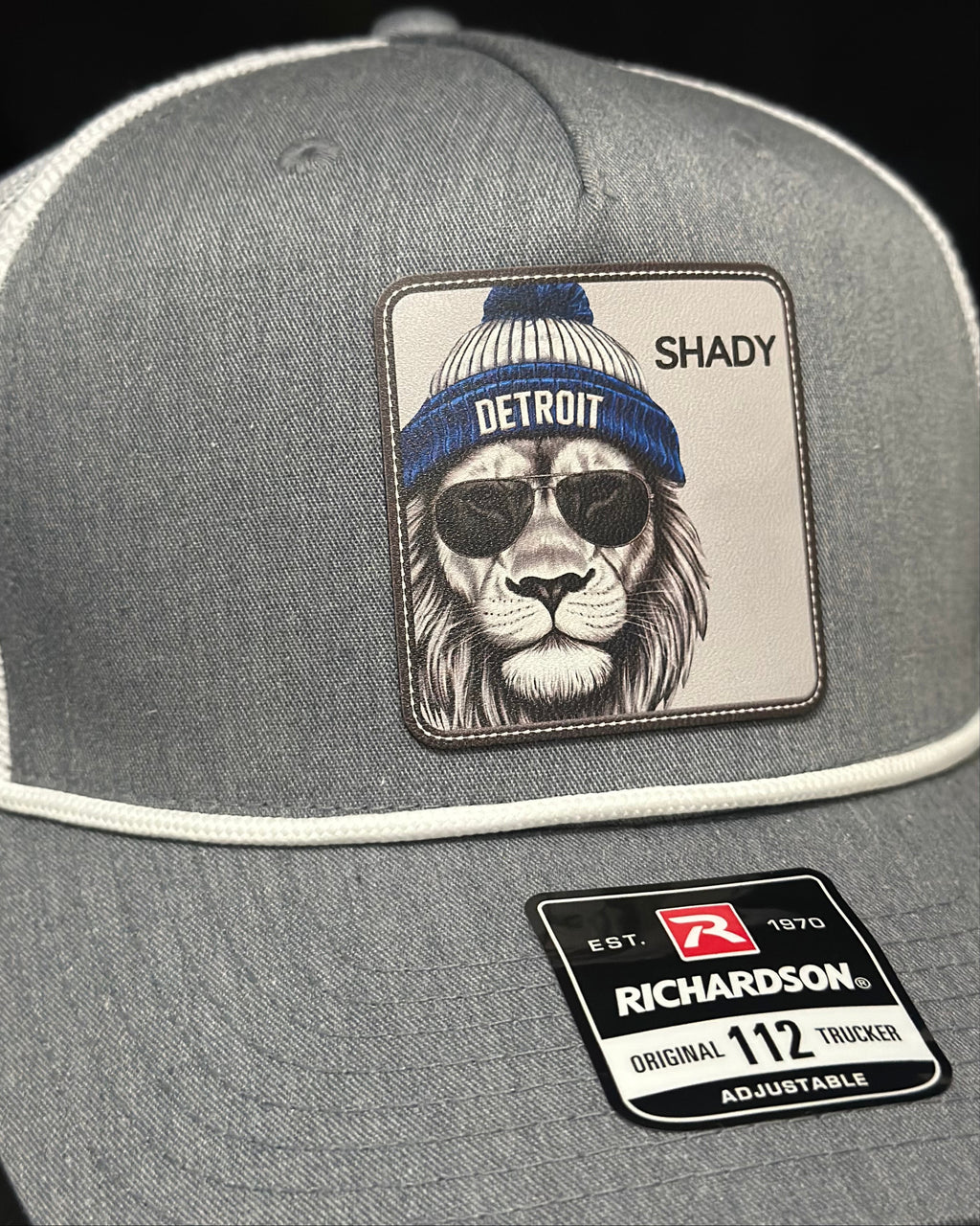 Gray trucker hat with a patch of a lion wearing sunglasses and a beanie, with 'Shady' text, and Richardson hat logo.